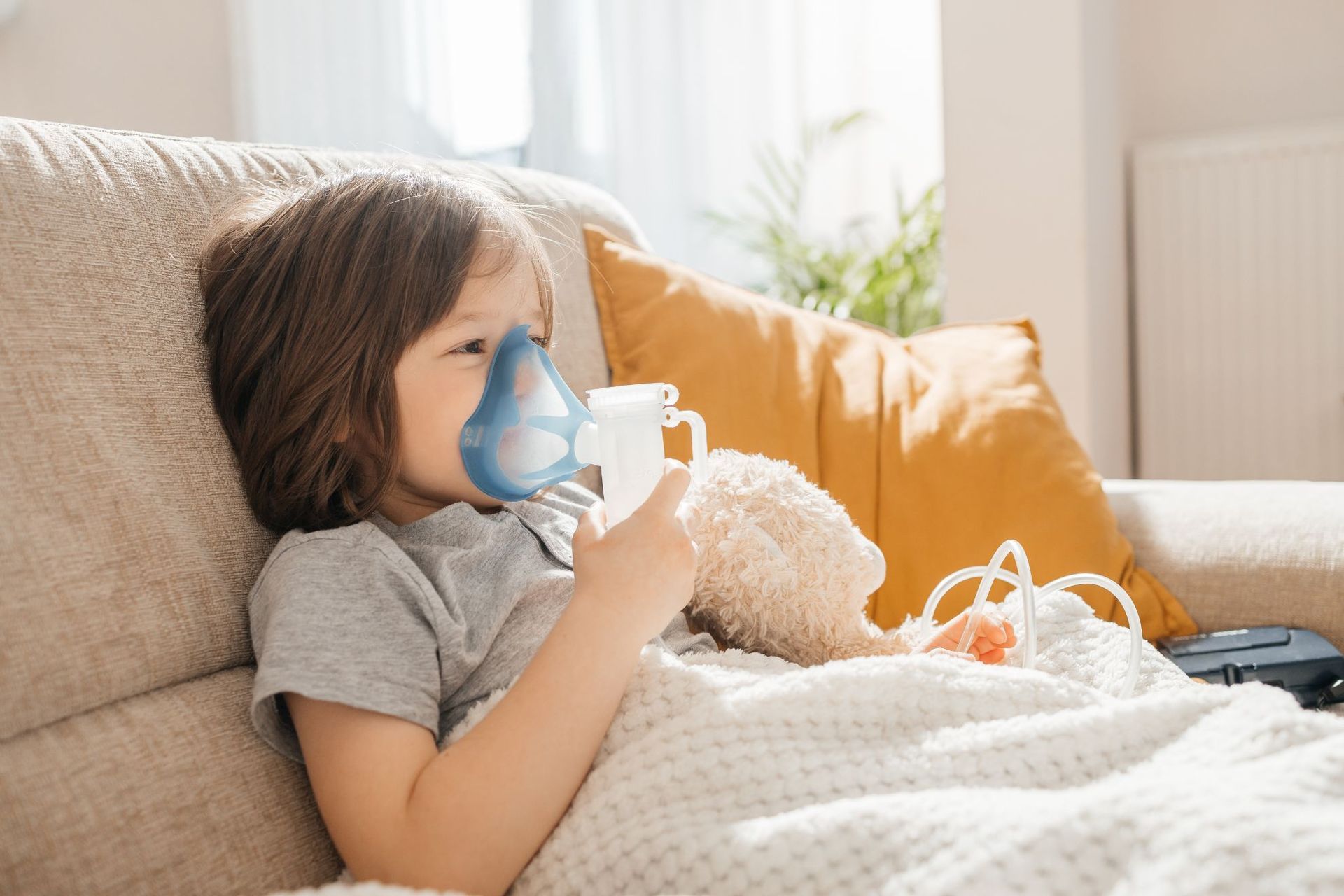 A young boy is using an inhaler while sitting on a couch.