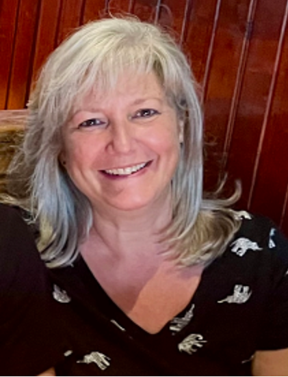 A woman with gray hair is smiling and wearing a black shirt